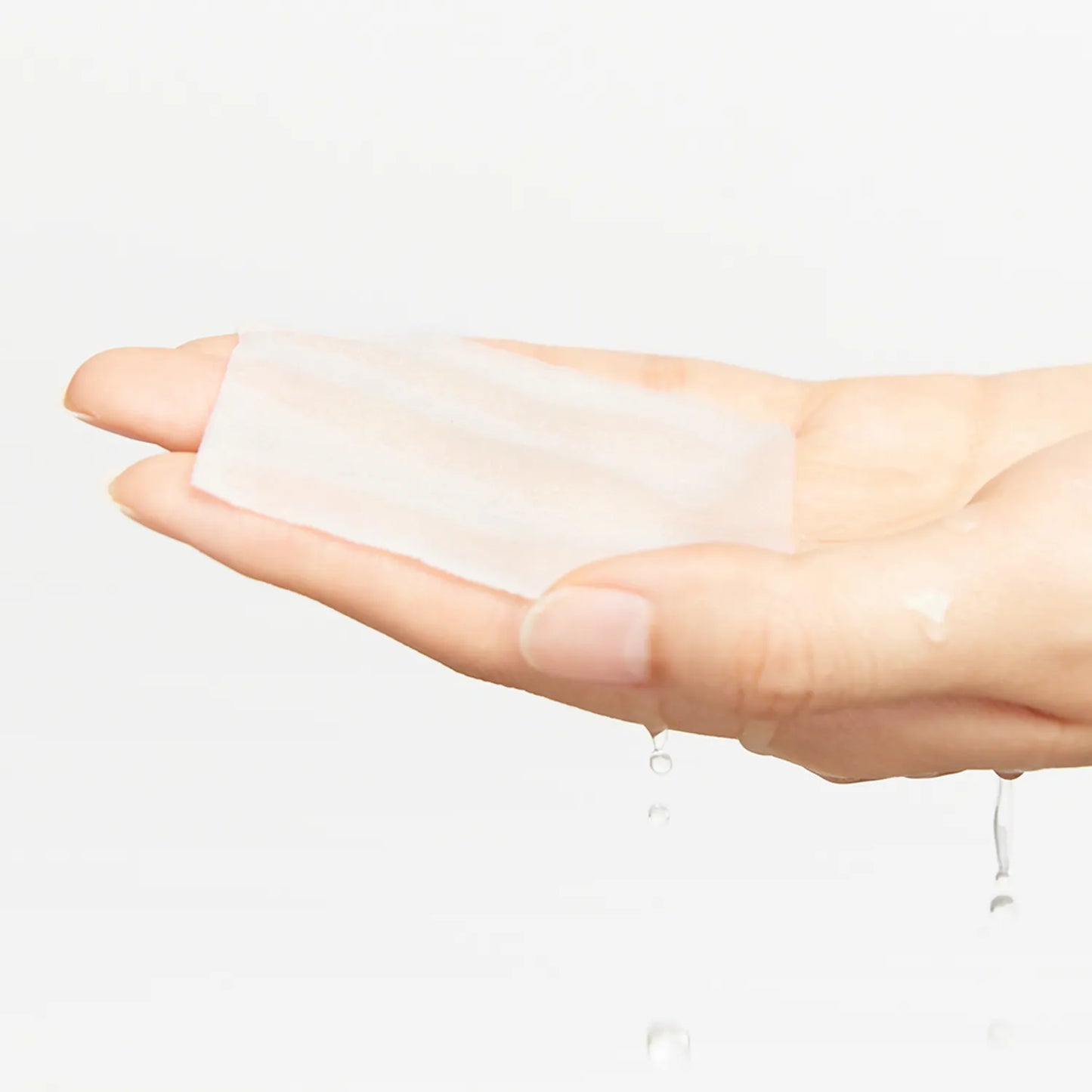 Hand holding a white patch with a small amount of liquid on a light gray background
