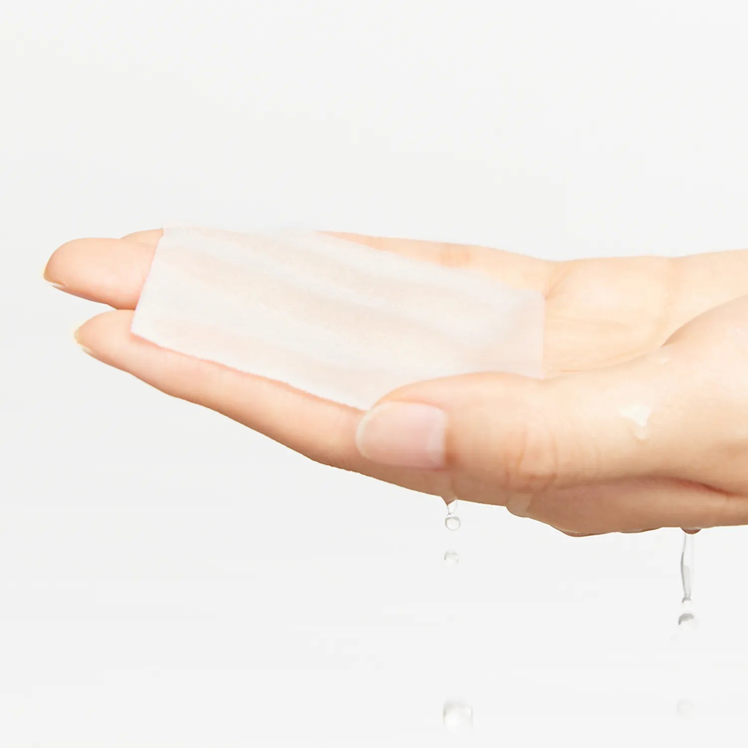 Hand holding a white patch with a small amount of liquid on a light gray background