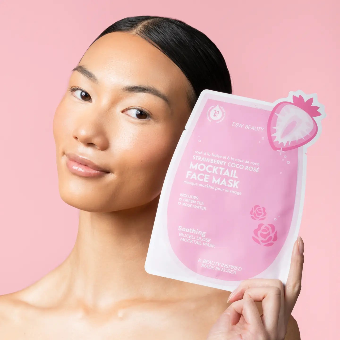 Woman holding a pink face mask package against a pink background