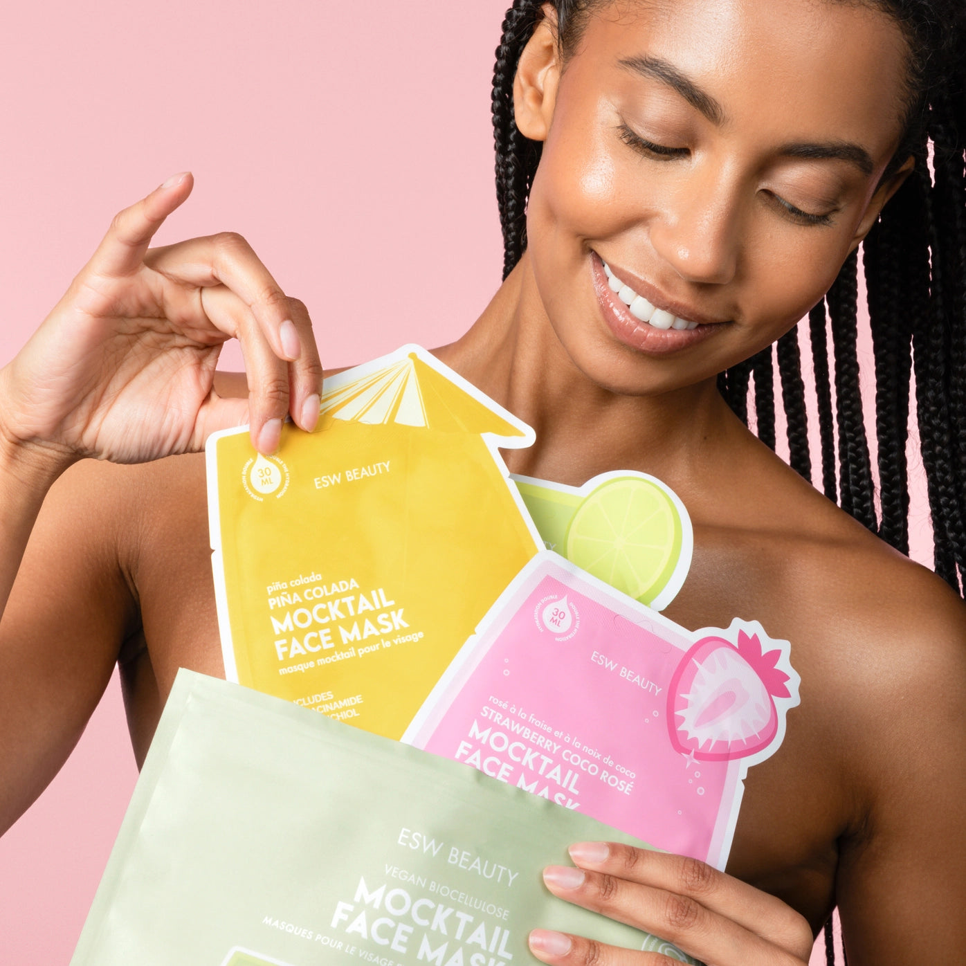Woman holding three colorful face mask packages against a pink background