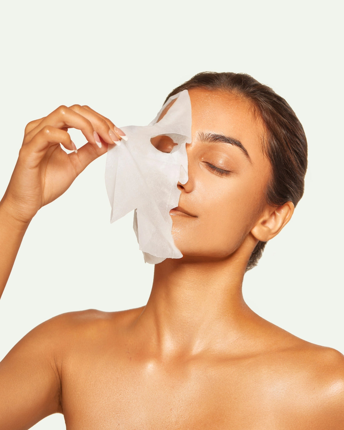 Woman applying a sheet mask to her face against a plain background